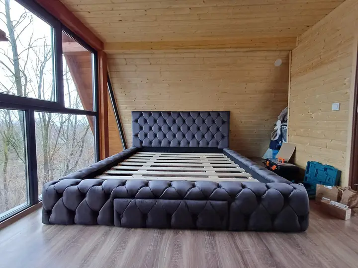 Pat tapițat model Chesterfield, catifea gri închis, montat într-o cabană din lemn